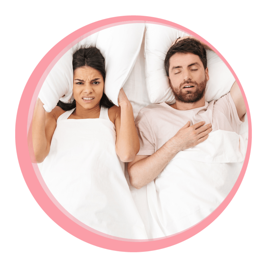 woman covering her ears with a pillow while man in bed beside her snores