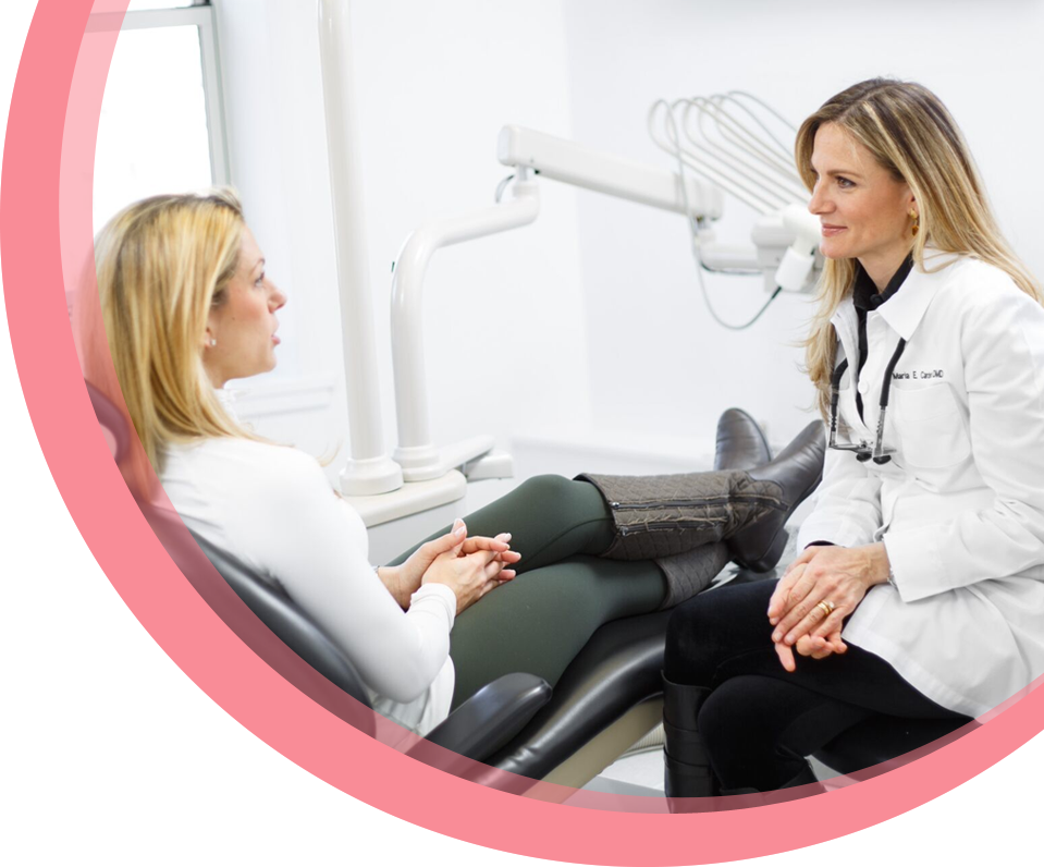 Dr Maria Cardenas sitting in a treatment room in the dental clinic in Wellesley and talking to a patient who is sitting in the dental chair.